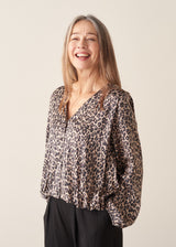 A woman wearing a satin leopard print blouse with a bubble hem and black trousers.