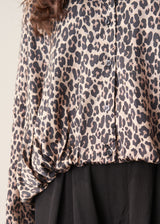 A woman wearing a satin leopard print blouse with a bubble hem and black trousers.
