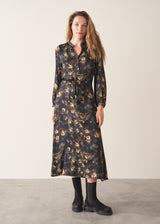 A woman wearing a dark floral satin midi dress with waist tie and button up detail and black chunky boots