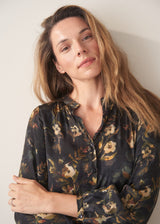 A woman wearing a dark floral satin midi dress with waist tie and button up detail and black chunky boots
