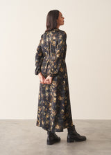 A woman wearing a long-sleeve, dark floral midi dress with a tie waist, set against a plain off-white studio background.