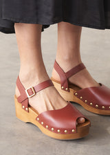 Brown wooden clogs with studded details worn by a person on a neutral background
