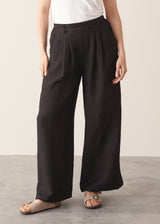 Woman wearing a white tank top and black wide-leg linen trousers against a plain background