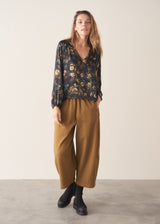 A woman wearing a long-sleeve dark floral blouse with a V-neckline, paired with mustard yellow drawstring barrel leg trousers