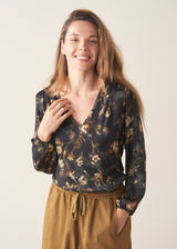 A woman wearing a long-sleeve dark floral blouse with a V-neckline, paired with mustard yellow drawstring barrel leg trousers