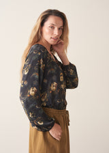A woman wearing a long-sleeve dark floral blouse with a V-neckline, paired with mustard yellow drawstring barrel leg trousers