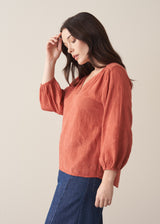 Woman wearing a terracotta cotton blouse with embroidered detail and blue jeans