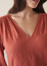 Woman wearing a terracotta cotton blouse with embroidered detail and blue jeans