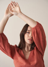 Woman wearing a terracotta cotton blouse with embroidered detail and blue jeans