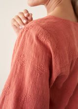 Woman wearing a pale terracotta cotton top with embroidery detail and a light linen skirt
