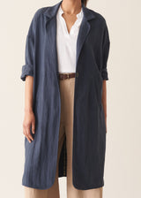 Woman wearing navy trench coat with light trousers and a white top