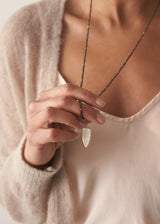 Close up of women wearing a smokey grey crystal beads, finished with white, quartz heart pendant, with a satin blouse