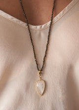 Close up of a smokey grey crystal beads, finished with white, quartz heart pendant, worn over a satin blouse