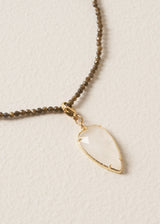 Close up of a smokey grey crystal bead necklace, finished with white, quartz heart pendant, on a beige background