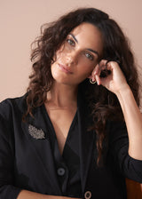 Model wearing a black blazer with a leaf brooch embellished with smoky-grey crystals, against a beige background