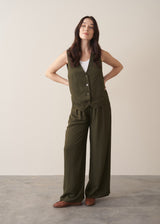 Woman wearing green waistcoat, green high waisted trousers and white vest top, styled with brown loafers against a beige background