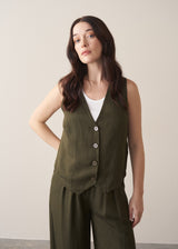 Woman wearing green waistcoat, green high waisted trousers and white vest top