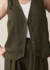 Close up of woman wearing a green waistcoat, green high waisted trousers and white vest top