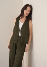 Woman wearing green waistcoat, green high waisted trousers and white vest top