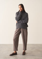 Woman wearing a dark grey high neck sweater with checked trousers against a plain background.