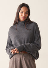 Woman wearing a dark grey high neck sweater with checked trousers against a plain background.