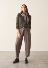 A woman wearing a dark khaki green sequin sweater with brown checked trousers and a black belt
