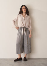 Woman wearing nude tie-front linen shirt with striped wide leg trousers.