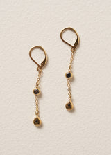 Delicate gold chain drop earrings featuring black crystals, set against a beige background