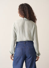 Person wearing a light green shirt and blue jeans against a plain background