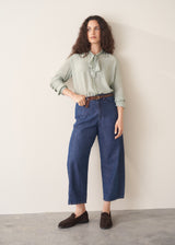 Woman wearing a light green blouse and blue jeans against a plain background