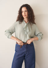 Woman wearing a light green blouse and blue jeans against a plain background