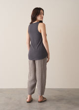 Woman wearing a dark grey tank top and checked linen trousers with sandals, against a plain background