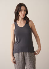 Woman wearing a dark grey tank top and checked linen trousers against a plain background