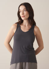 Woman wearing a dark grey tank top and checked linen trousers against a plain background