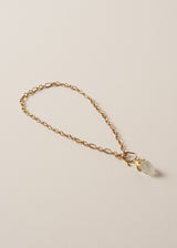 Gold chain necklace with a clear chunky crystal pendant on a beige background