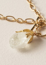 Gold chain necklace with a clear crystal chunky pendant on a beige background
