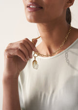 Woman in a light blue top wearing and holding a chunky gold chain necklace with a clear crystal pendant
