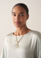 Woman in a light blue top wearing a chunky gold chain necklace with a clear crystal pendant