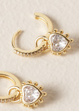 Close up of gold hoop earrings with heart-shaped gemstones on a beige background