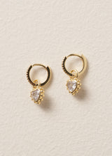 Gold hoop earrings with dainty heart-shaped gemstones on a beige background
