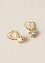 Gold hoop earrings with heart-shaped gemstones on a beige background