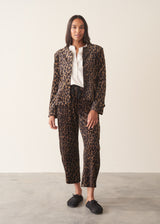 A woman wearing leopard-print velour trousers with a drawstring waist, paired with a white blouse and black slip-on shoes.