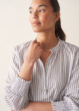 Woman wearing white and blue stripe light shirt with ruffle collar and red linen shorts