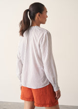Woman wearing white and blue stripe light shirt with ruffle collar and red linen shorts