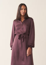 Woman wearing long sleeve plum satin button up dress with waist tie