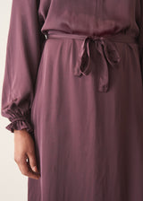 Woman wearing long sleeve plum satin button up dress with waist tie