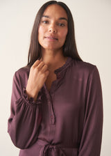 Woman wearing long sleeve plum satin button up dress with waist tie