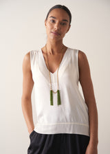 Model wearing a long, chunky chain necklace with two pendants made of colourful green crystal strands, with a white satin top, photographed against a beige background