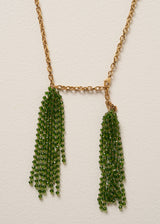 Close up detail of a long, chunky chain necklace with two pendants made of colourful green crystal strands, photographed on a beige background