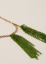 Close up detail of a long, chunky chain necklace with two pendants made of colourful green crystal strands, photographed on a beige background